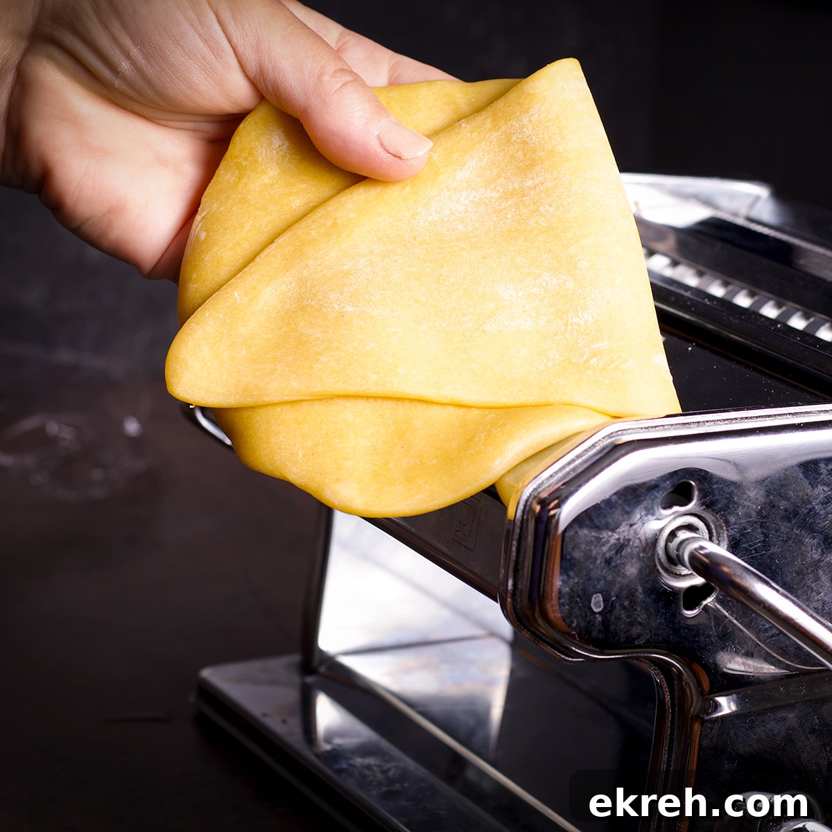 Folding a piece of pasta dough in half before feeding it back through the rollers of a pasta machine.