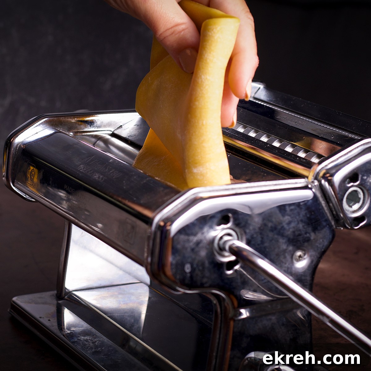 Rolling a piece of pasta dough through the rollers of a pasta maker.