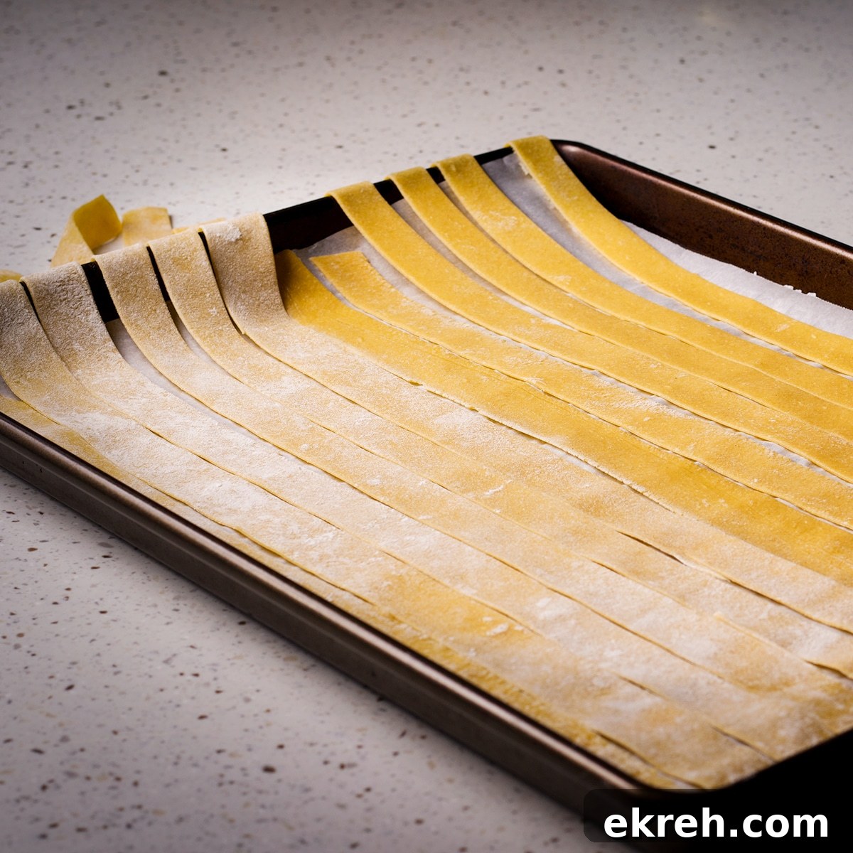Homemade pappardelle noodles laid out across a parchment paper lined baking sheet.