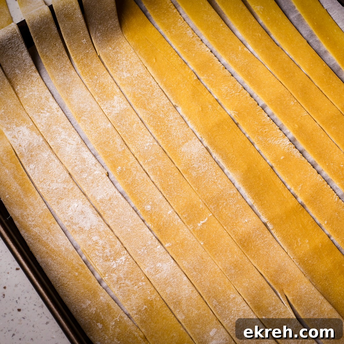 Homemade pappardelle noodles laid out across a parchment paper lined baking sheet.