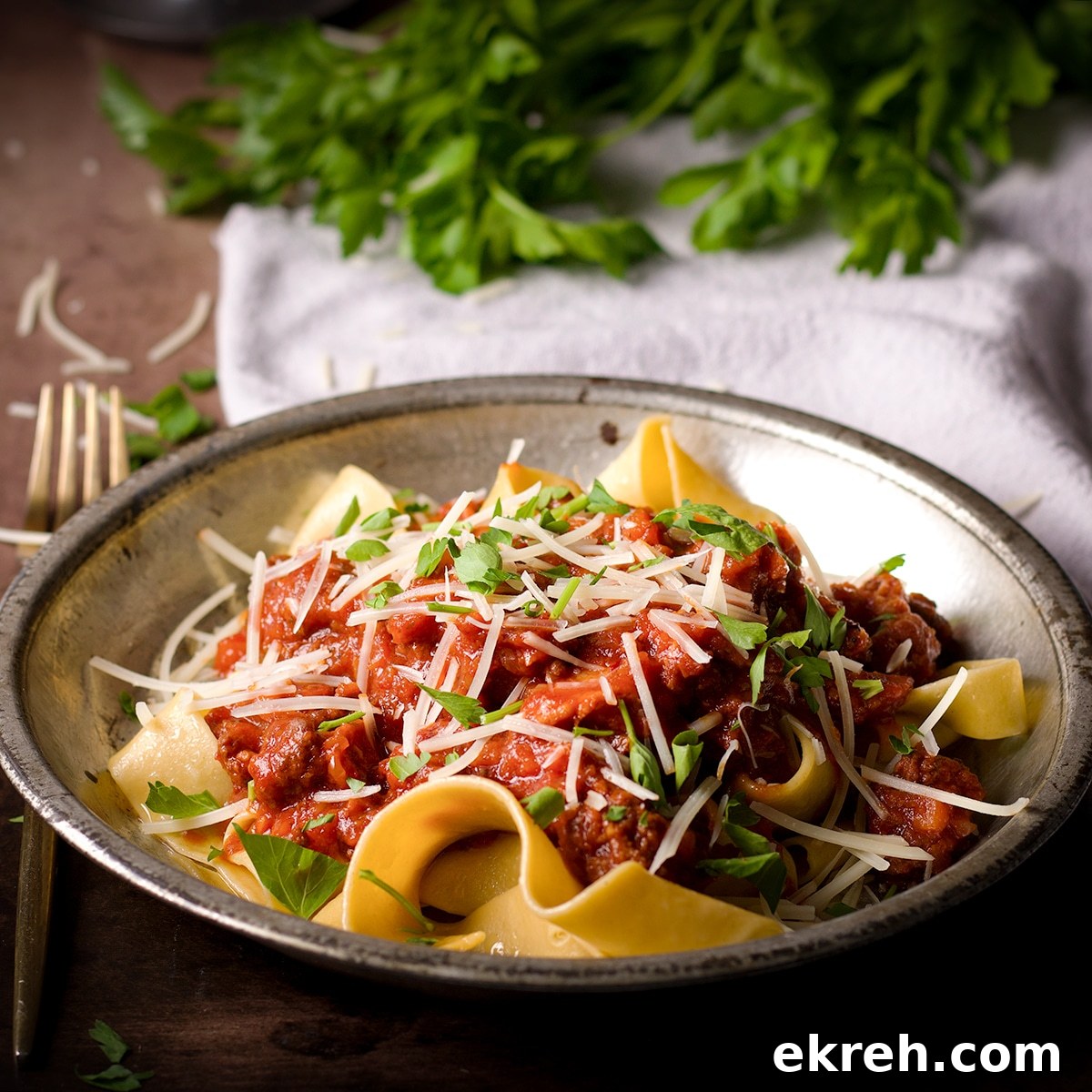 A plate filled with homemade pappardelle noodles covered in bolognese sauce.