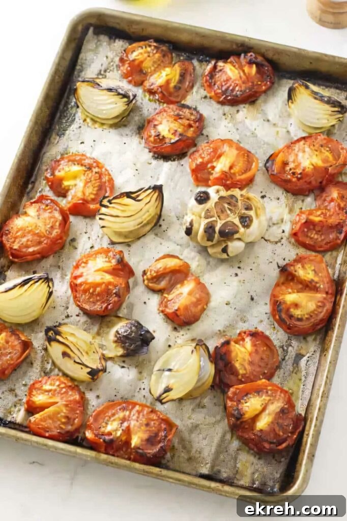 Roasted tomatoes and onions on a baking sheet.