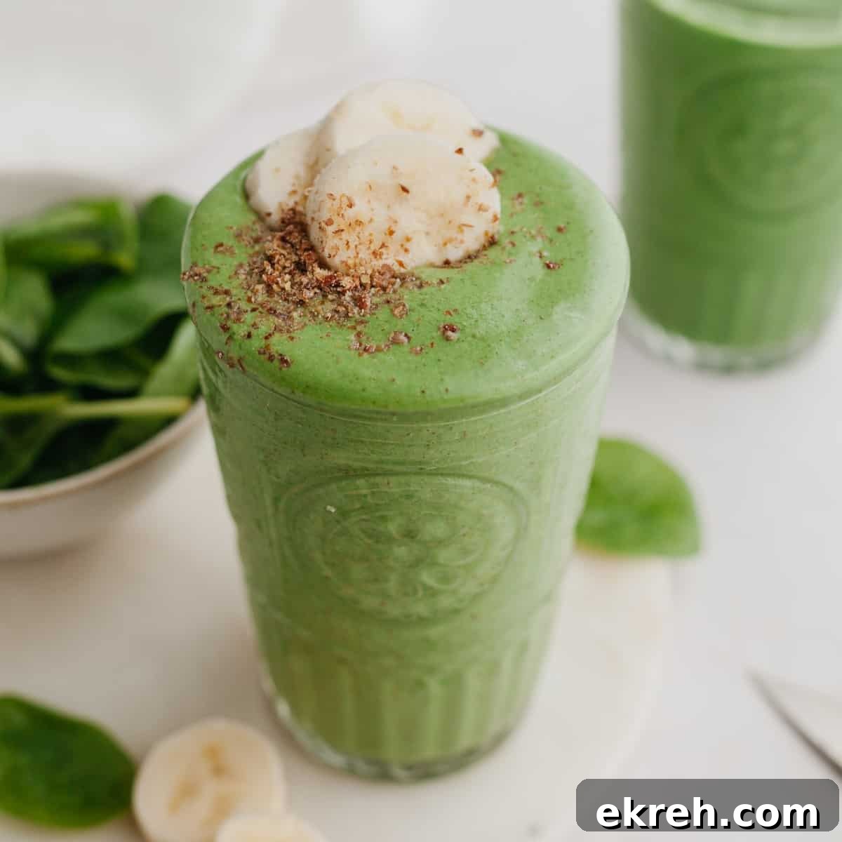 A large glass with a green smoothie in it, it is topped with banana slices.