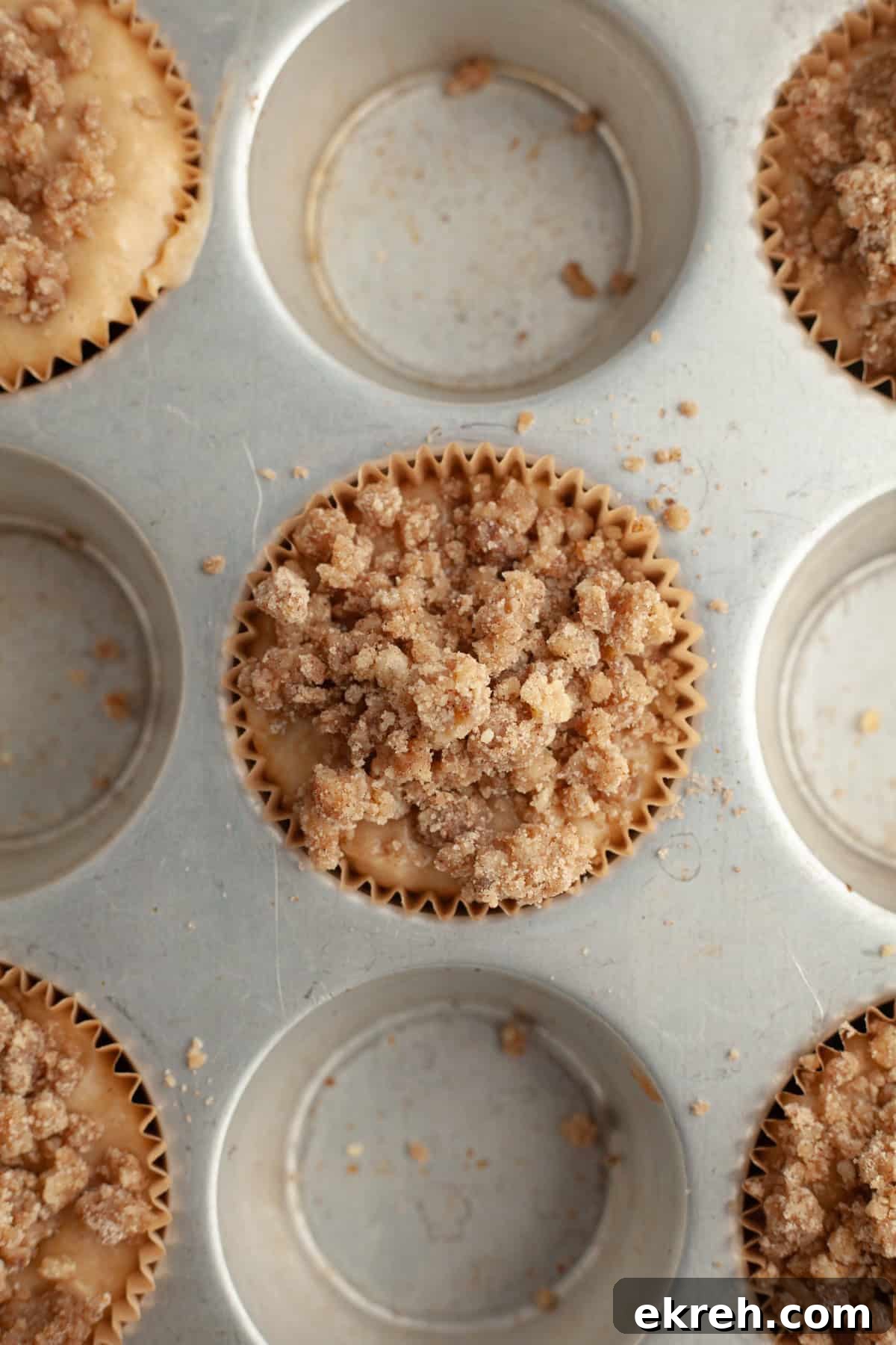 A muffin pan with unbaked banana muffins covered with streusel topping.