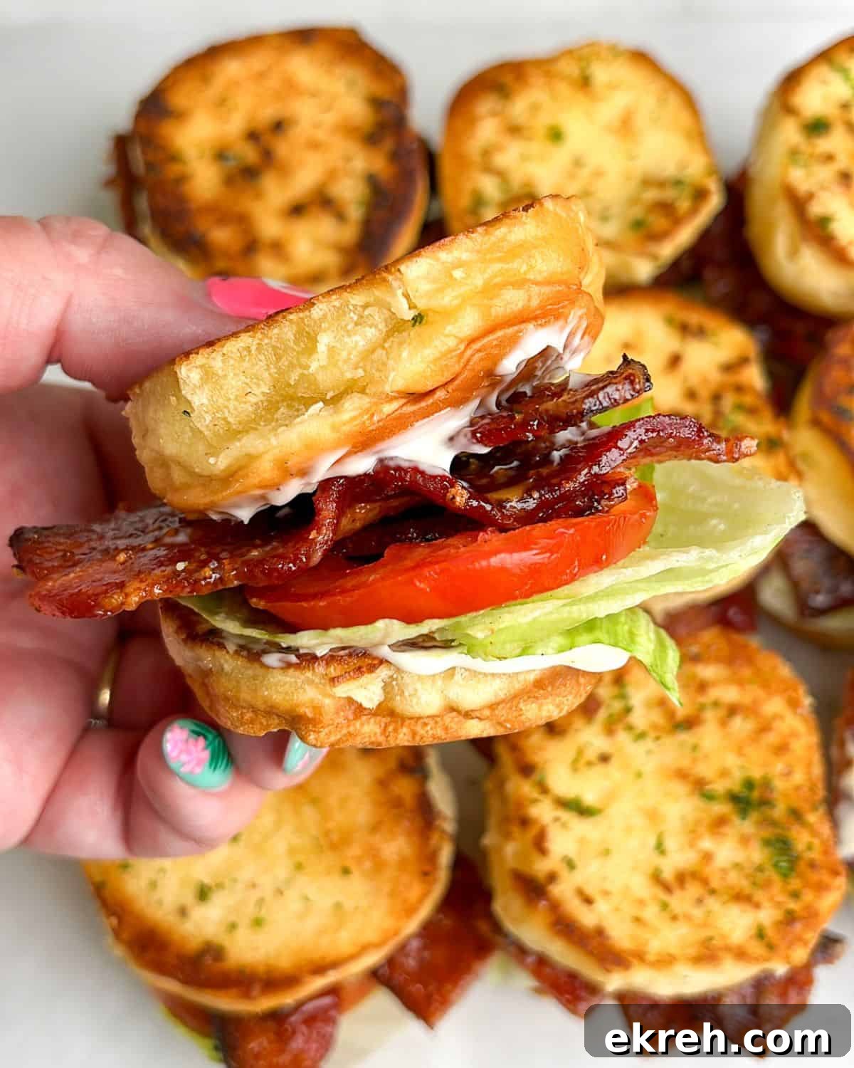 Candied Bacon BLT Sliders with Maple Glaze 4 blt sliders sitting on the table and held in hand