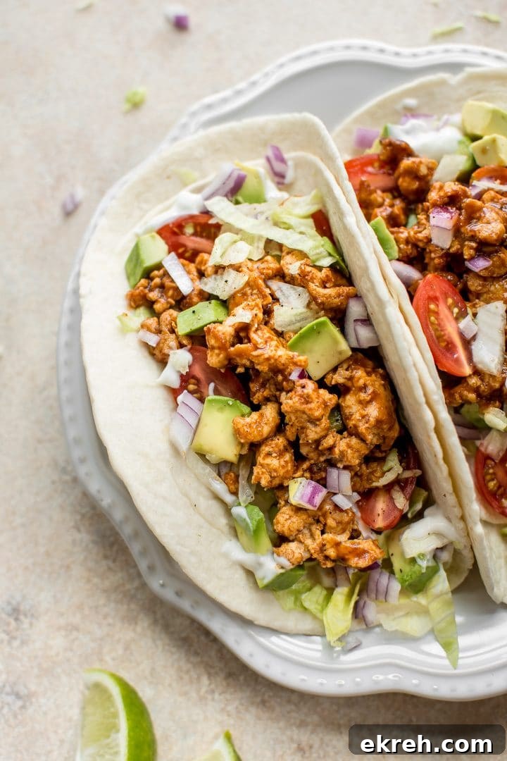 Close-up of BBQ chicken tacos with sour cream, onions, iceberg lettuce, and tomatoes on a plate