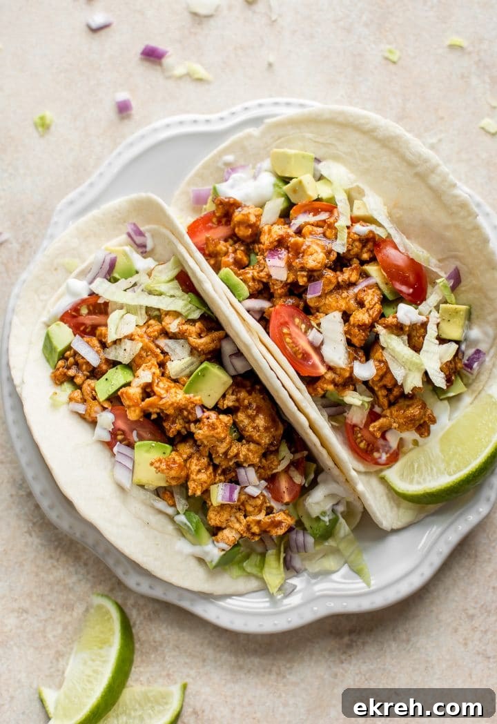 White plate with two BBQ chicken tacos topped with avocado, sour cream, onions, and lettuce