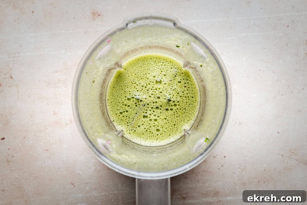 Top view of a blender containing jalapeño chile vinaigrette, likely a smoothie or juice, on a light-colored countertop.