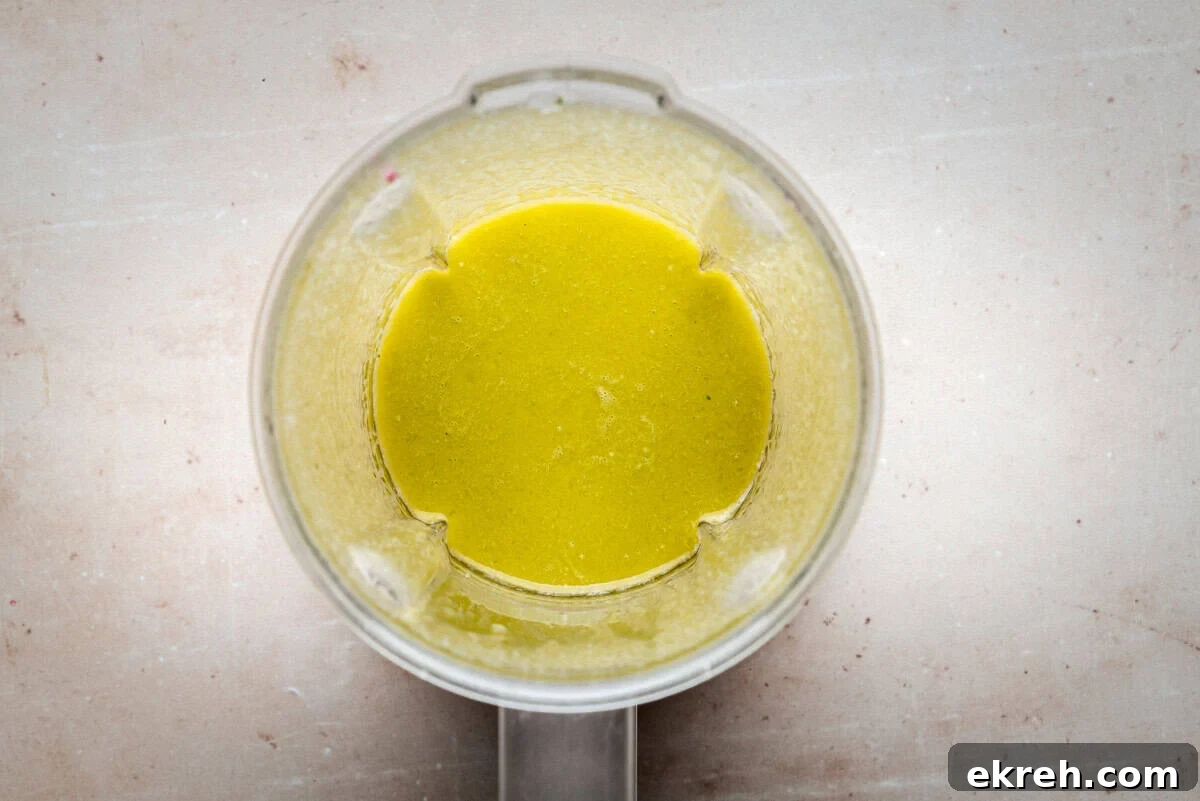 A top-down view of a blender containing a smooth, yellow-green liquid mixture, set on a light, speckled countertop.