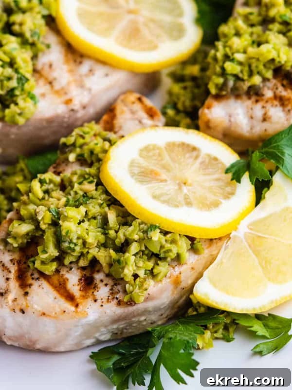 Grilled Swordfish served on a platter and topped with green olive tapenade, lemon slices and parsley.
