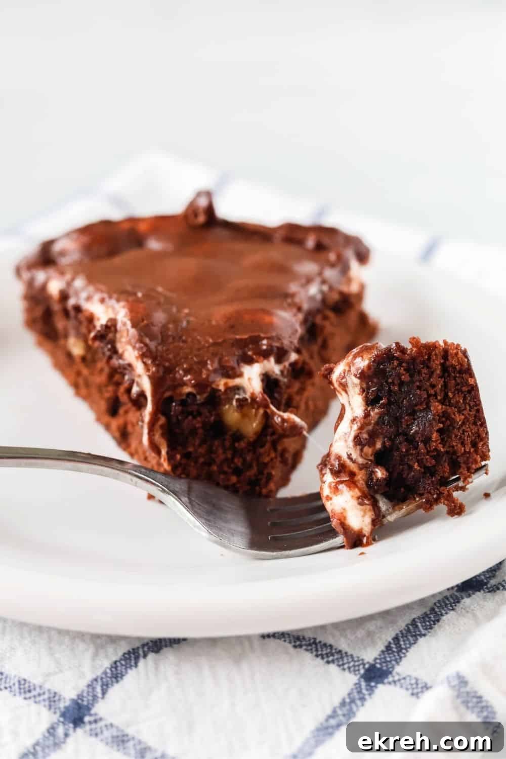 Classic Appalachian Fudge Brownie Pie Recipe 5 a fork holds a bite of Appalachian fudge brownie pie, with the remaining slice of pie behind it on a white plate.