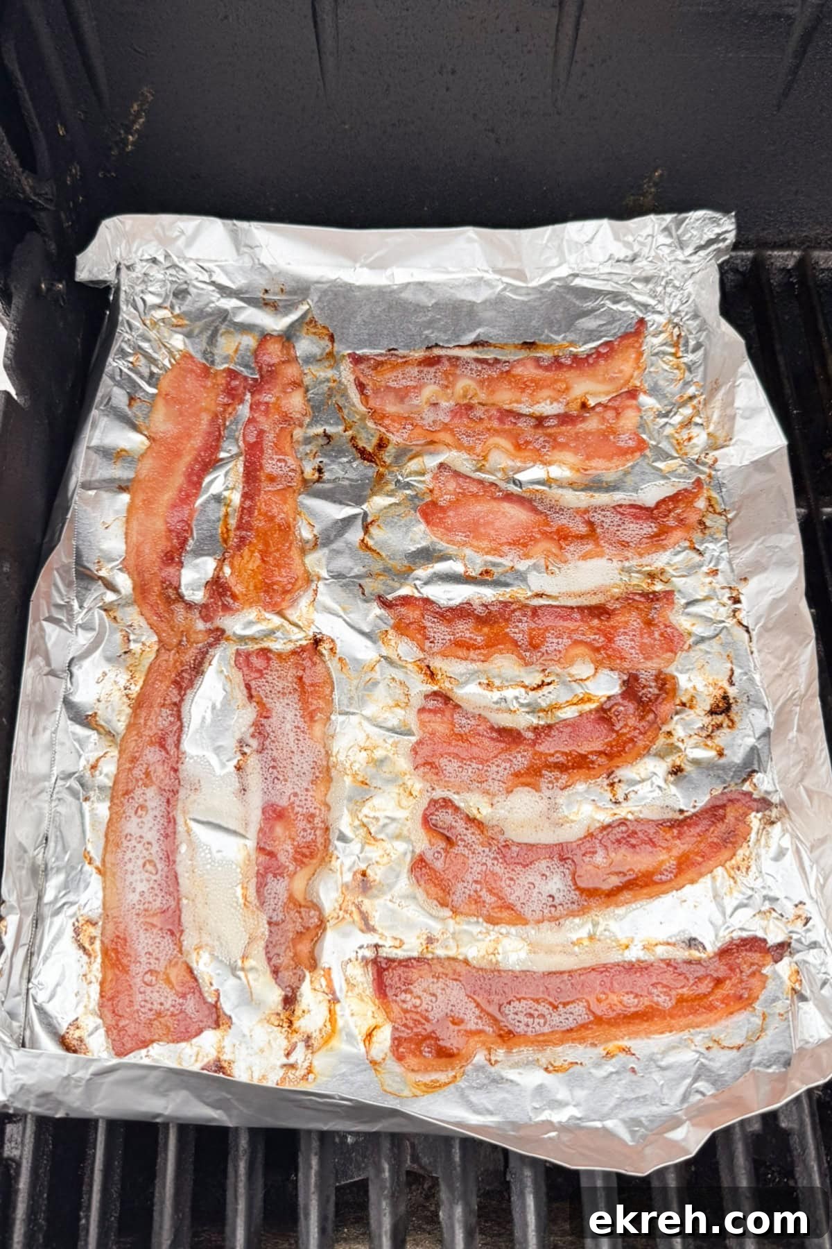 Juicy Grilled Bacon Cheeseburgers with Beef and Pork Patties 16 Several strips of cooked bacon are laid out on a sheet of aluminum foil, which is placed on a grill. The bacon is sizzling with visible grease and crispy edges.