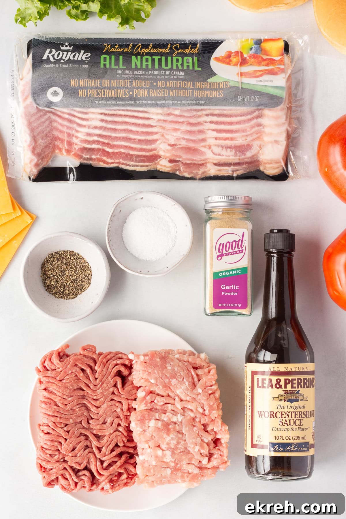 Juicy Grilled Bacon Cheeseburgers with Beef and Pork Patties 3 A flat lay of ingredients including a package of bacon, ground beef, ground pork, a bottle of Worcestershire sauce, a jar of garlic granules, black pepper, salt, and slices of tomato and cheddar cheese.