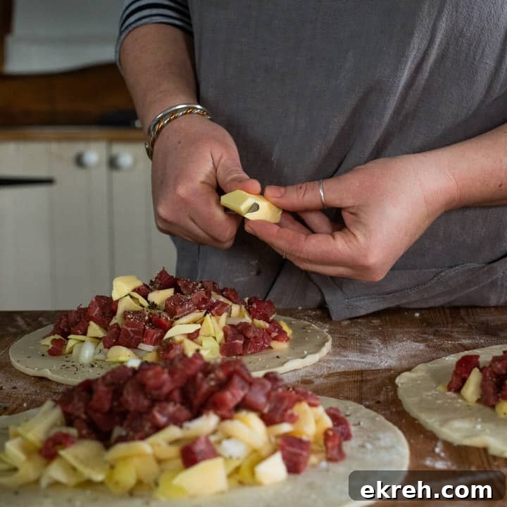 How to Make a Traditional Cornish Pasty (Authentic Recipe) 10 womans hands chopping a piece of butter up over the top of three pasties that are about to be crimped