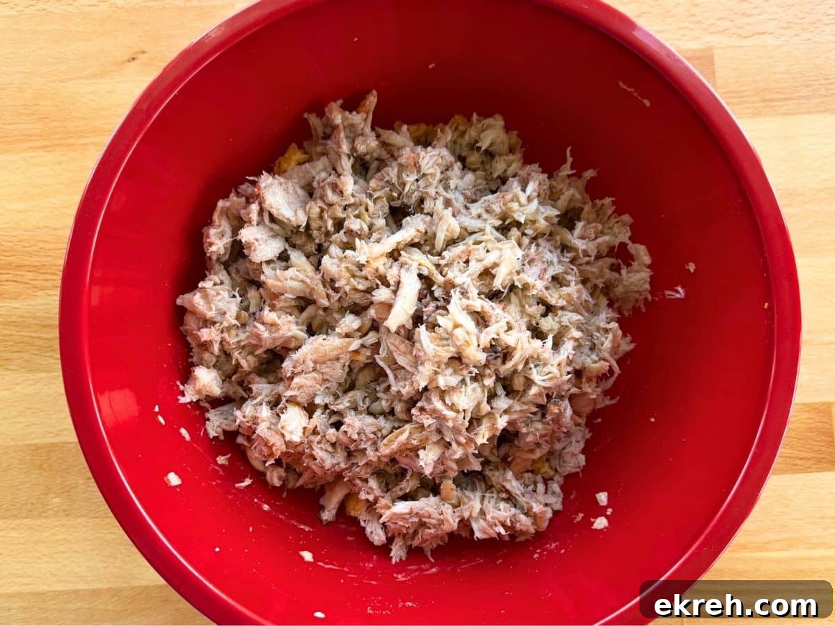 Lump crab, broken into chunks and folded into binder ingredients in a red bowl.