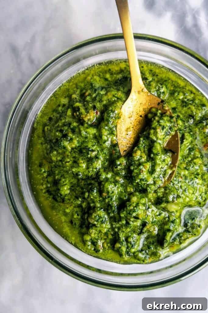 Basil pesto in a small glass bowl, with a gold spoon on a grey marble background.