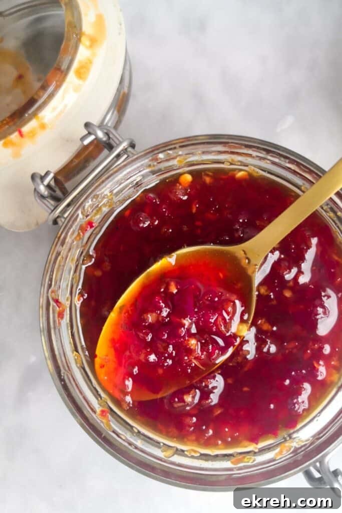 Close up, over head shot of chilli jam in a glass jar, with a gold spoon picking up some jam.