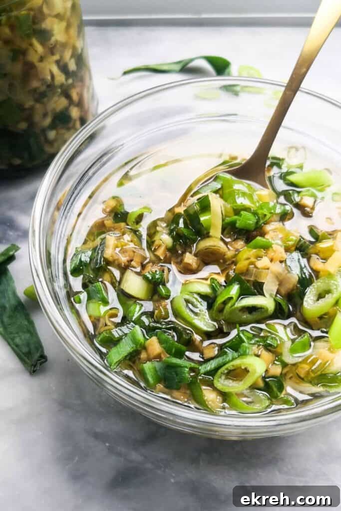 Ginger and spring onion oil in a small glass bowl, with a glass jar of oil in the background.