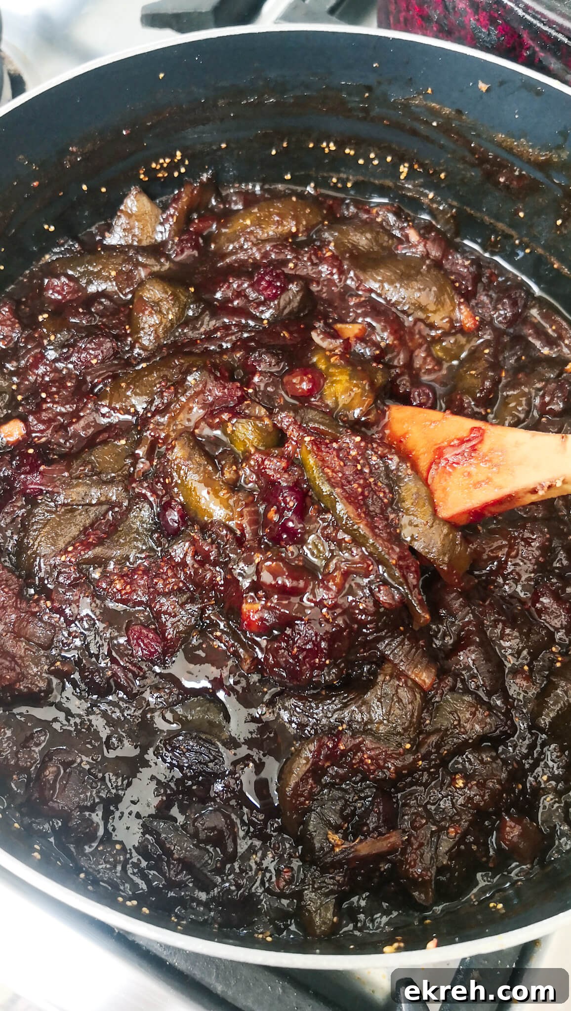 A large wooden spoon stirring fig chutney in a large pot.