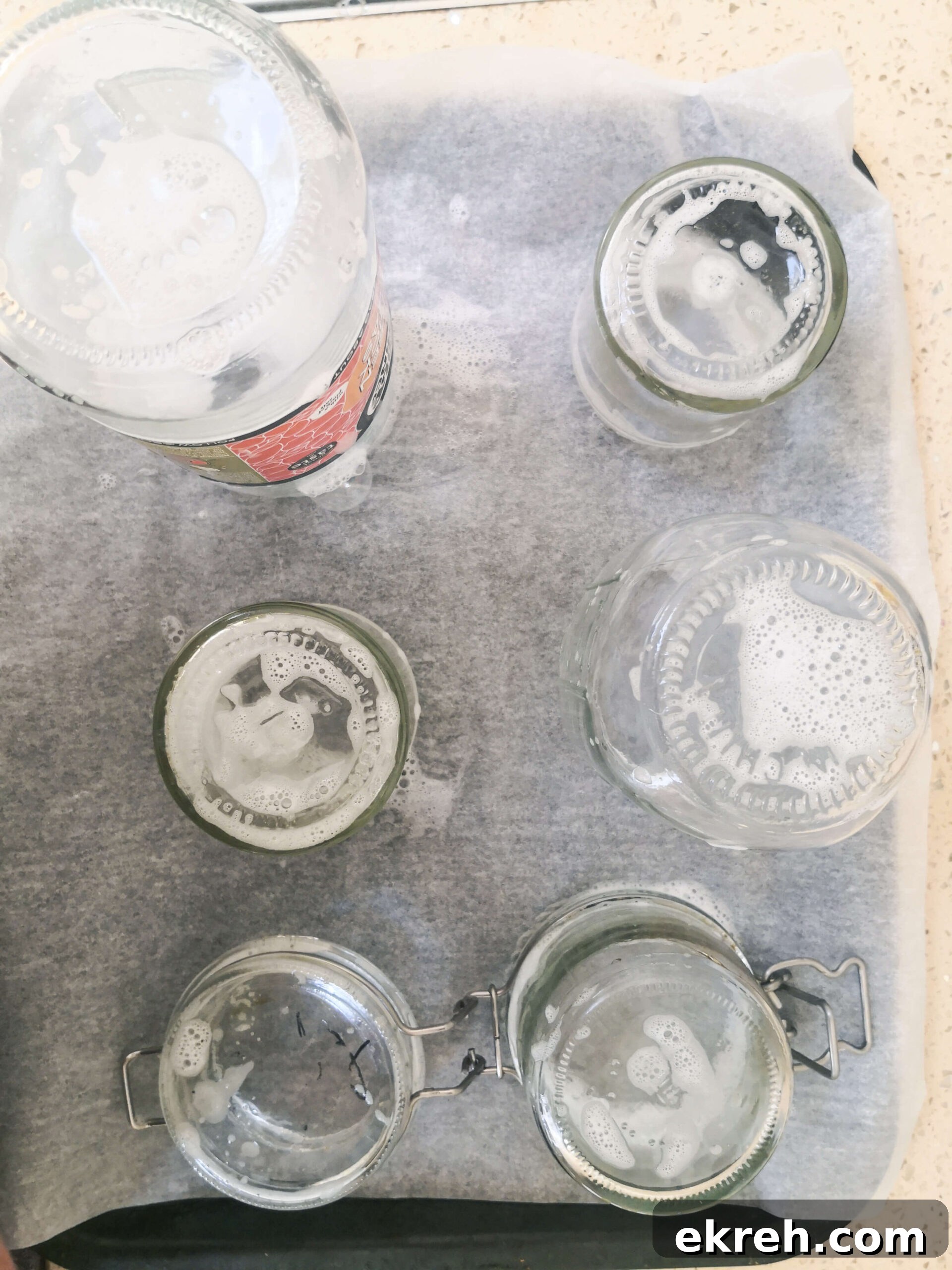 Soapy glass jars standing upright on a lined oven tray.