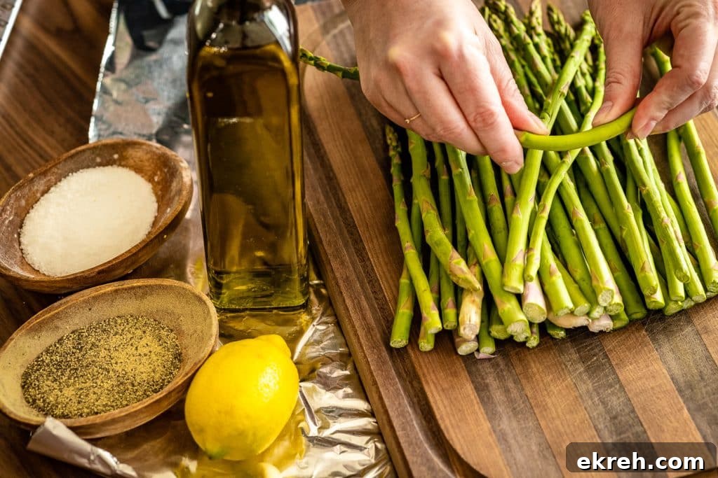 Trimmed asparagus on a wooden cutting board next to salt pepper, olive oil, and lemon.