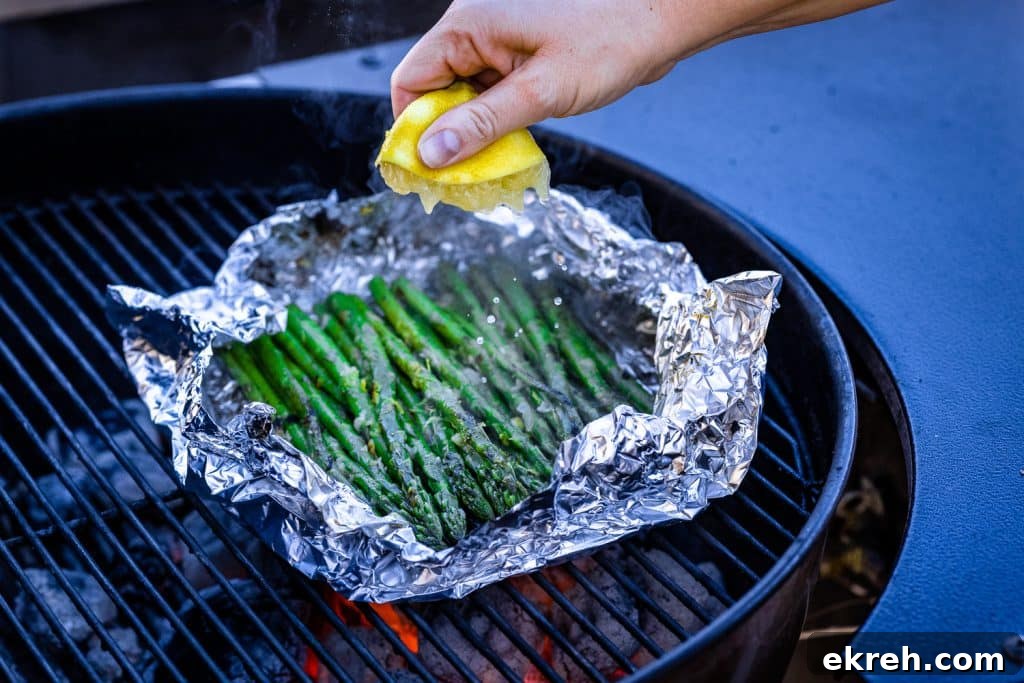 Fresh lemon being squeezed over grilled asparagus in foil.