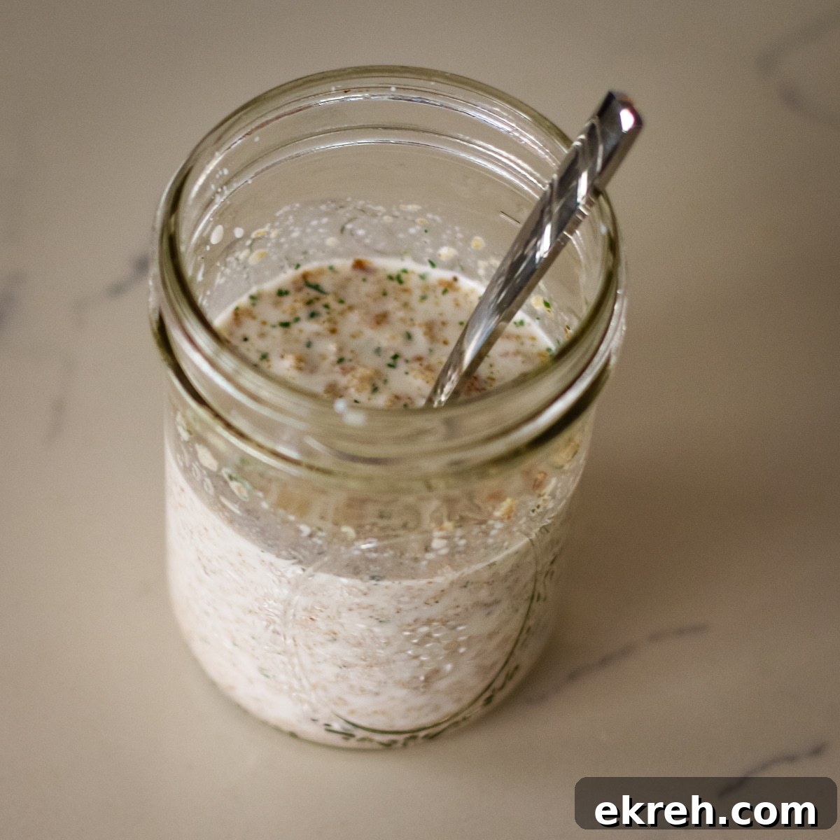 overhead shot of a glass jar filled with creamy mixture, with a metal spoon inside.
