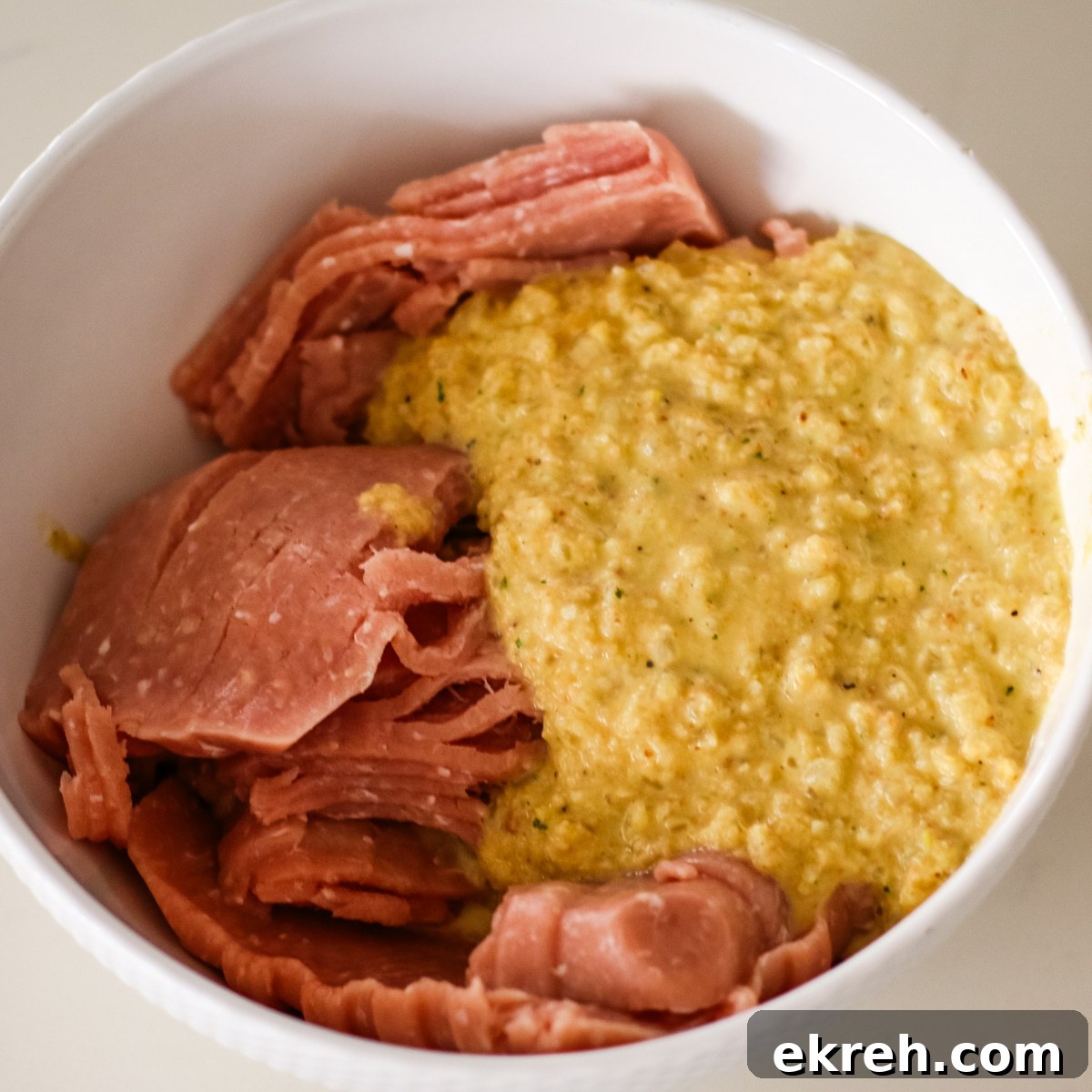 close-up of ground chicken slices and a yellow, wet bread binder in a white mixing bowl.