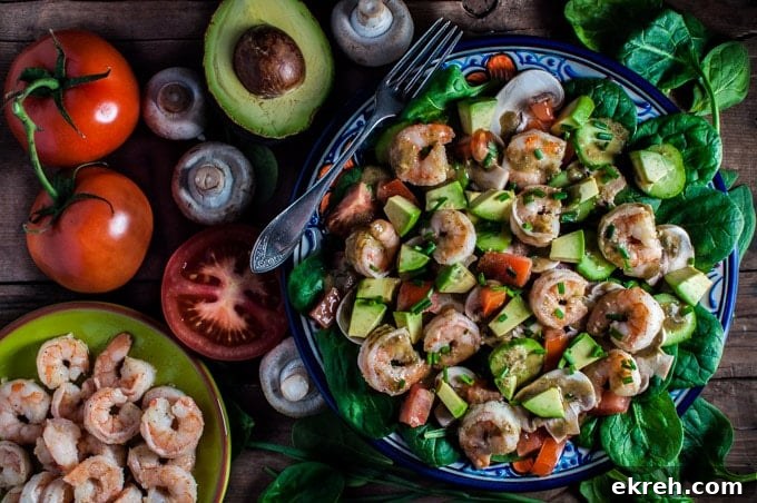 plate with spinach salad with shrimp and a smoky sweet dressing with several ingredients beside it