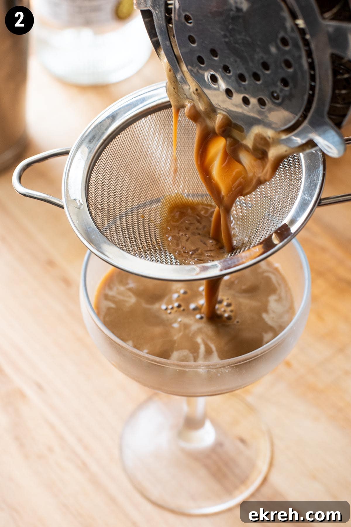 Double straining a chocolate espresso martini into a chilled coupe glass.