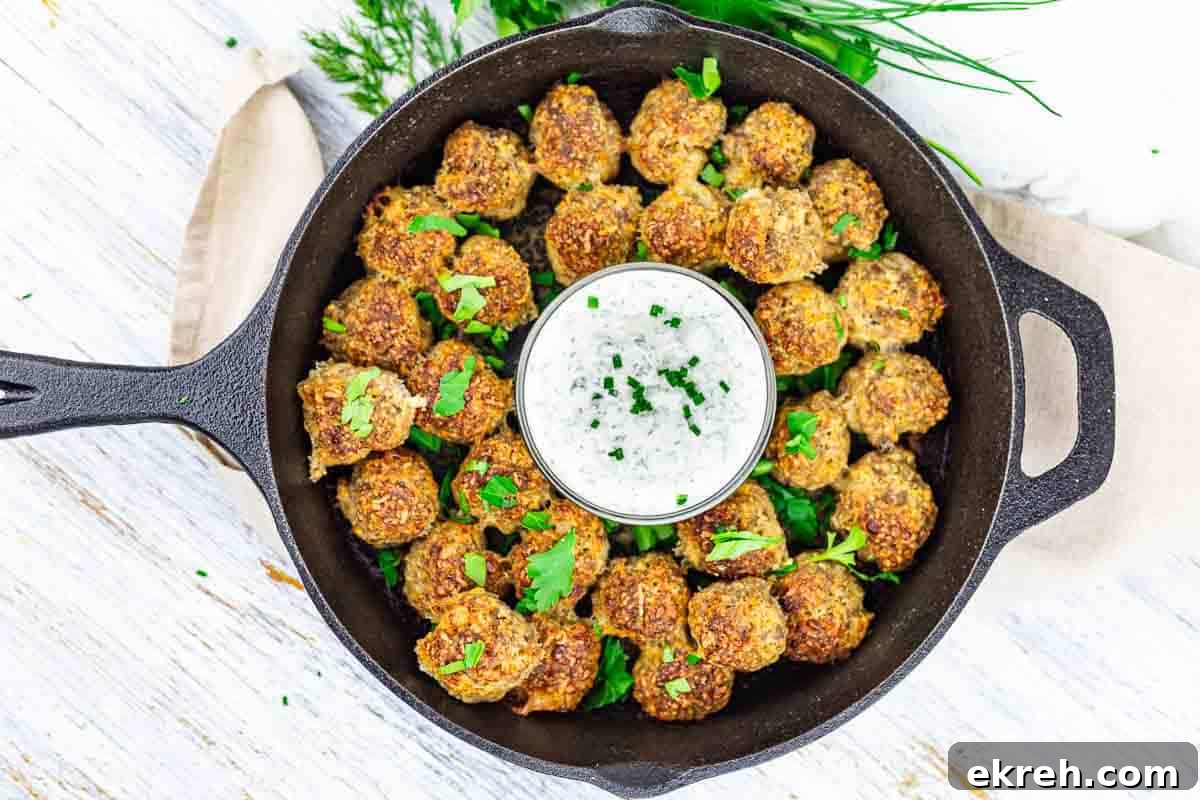 Cast iron skillet with cream cheese sausage balls arranged around a bowl of white dip, garnished with chopped herbs.