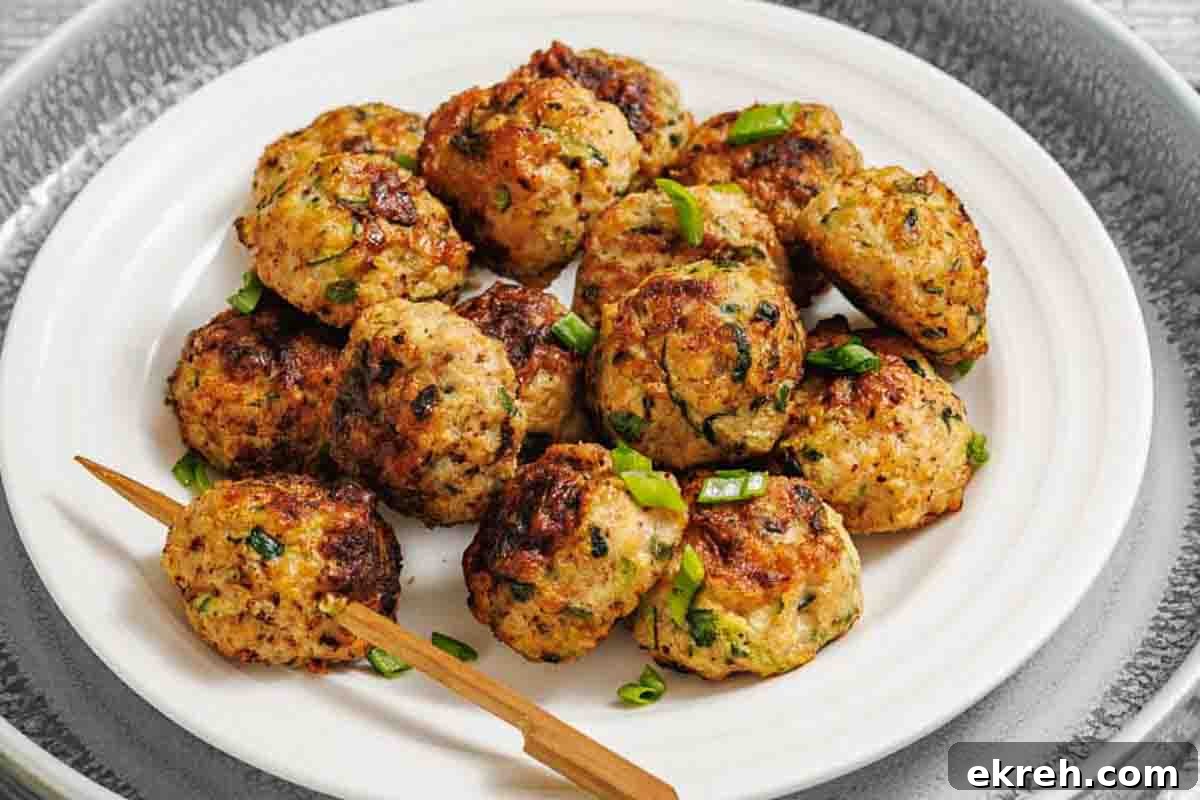 A white plate with several zucchini patties garnished with chopped green onions, and a wooden skewer resting on the edge.