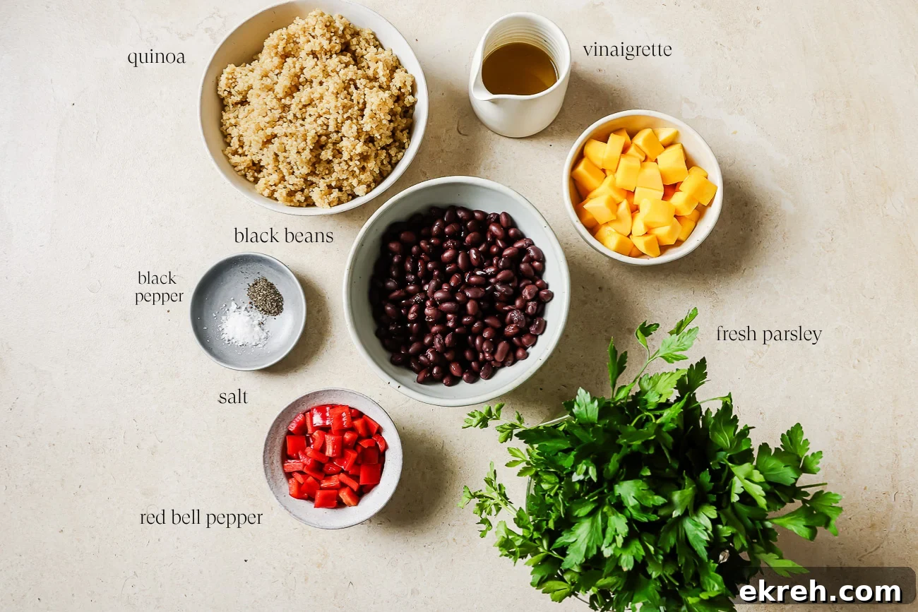 Bowls of mango quinoa salad with black beans, diced red bell pepper, salt, black pepper, a cup of vinaigrette, and a bunch of fresh parsley arranged on a light surface.