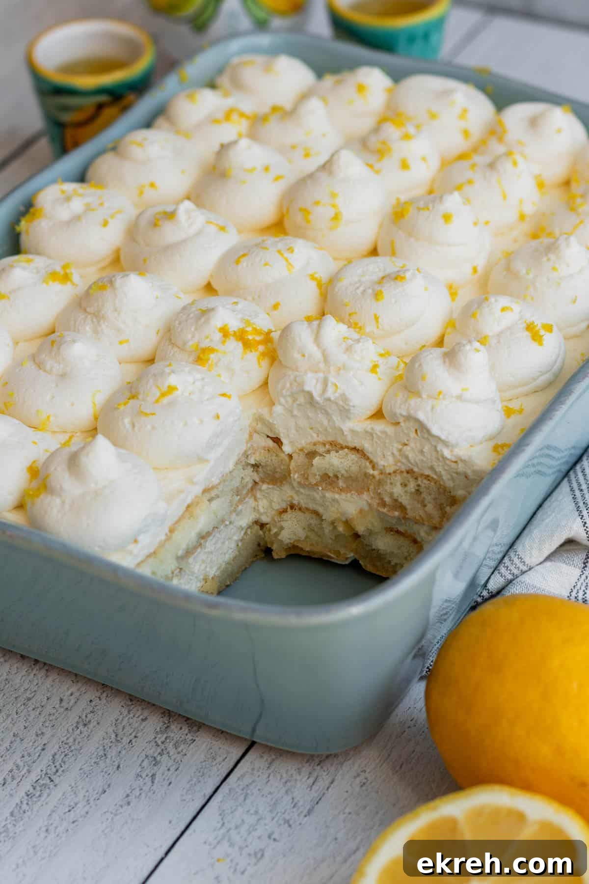 Limoncello Tiramisu Recipe with Zesty Lemon Mascarpone 2 blue baking dish with layers of ladyfingers and lemon mascarpone with lemons to side of baking dish