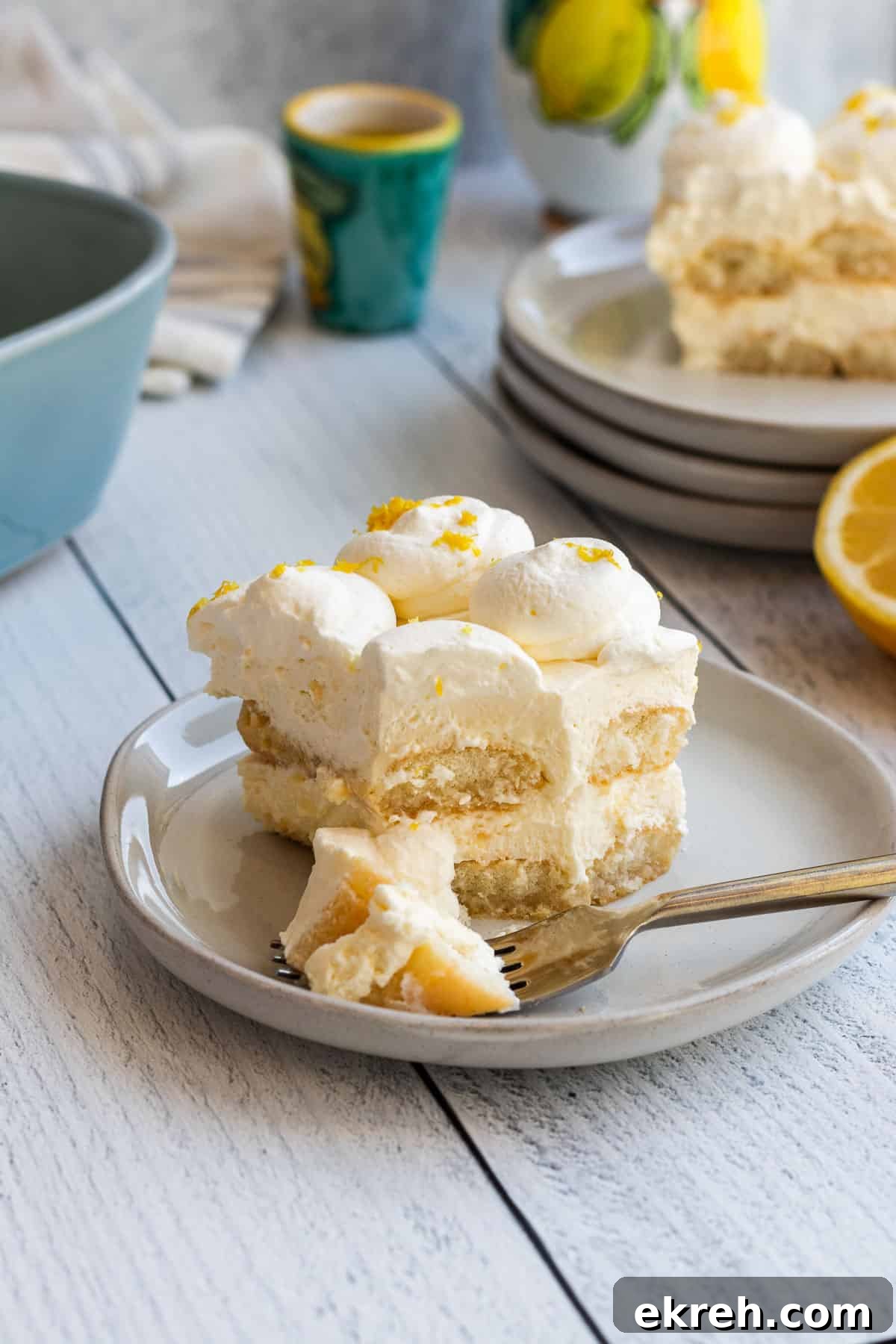 Limoncello Tiramisu Recipe with Zesty Lemon Mascarpone 4 plate of limoncello tiramisu with a gold fork of tiramisu and a stack of plates and another slice of tiramisu in the background
