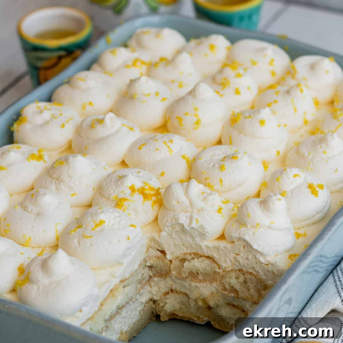 blue baking dish with layers of ladyfingers and lemon mascarpone with lemons to side of baking dish