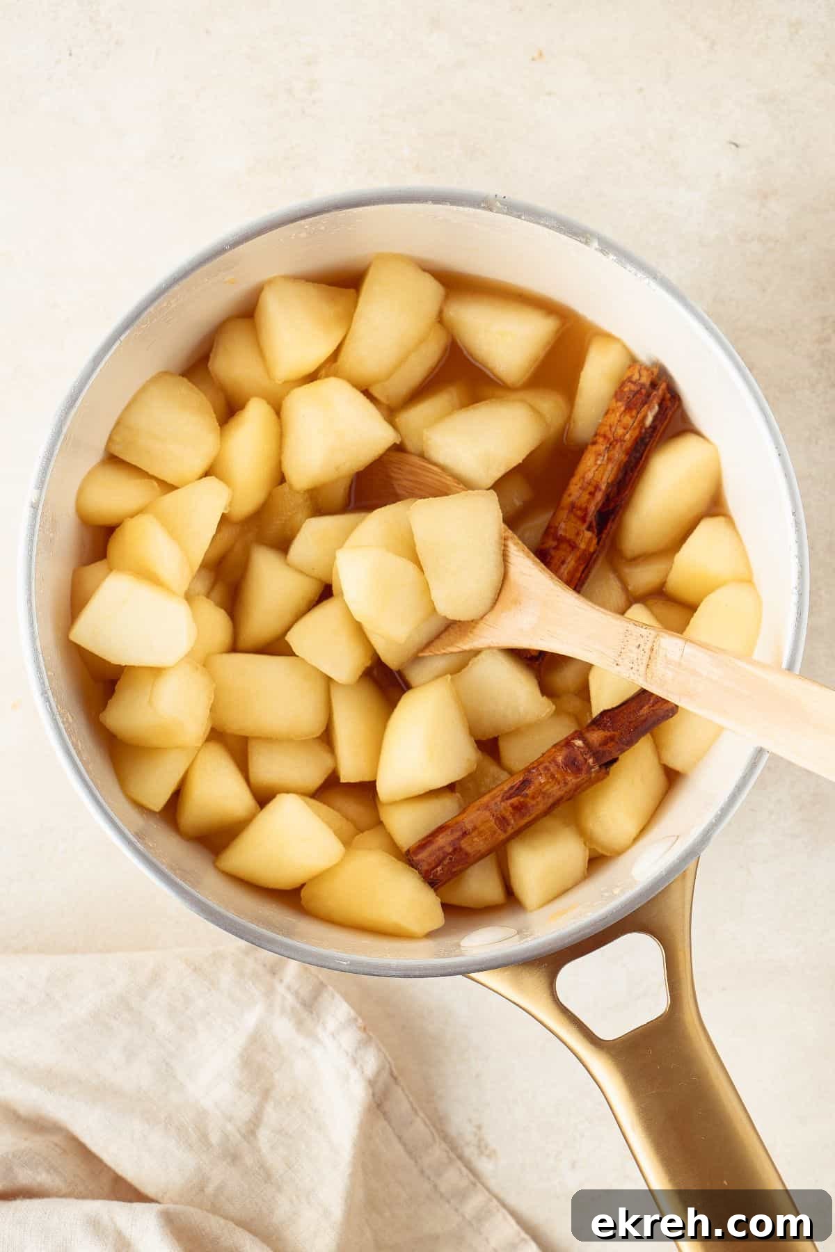 Stewed Apples in a saucepan, with a wooden spoon sitting in the pan.