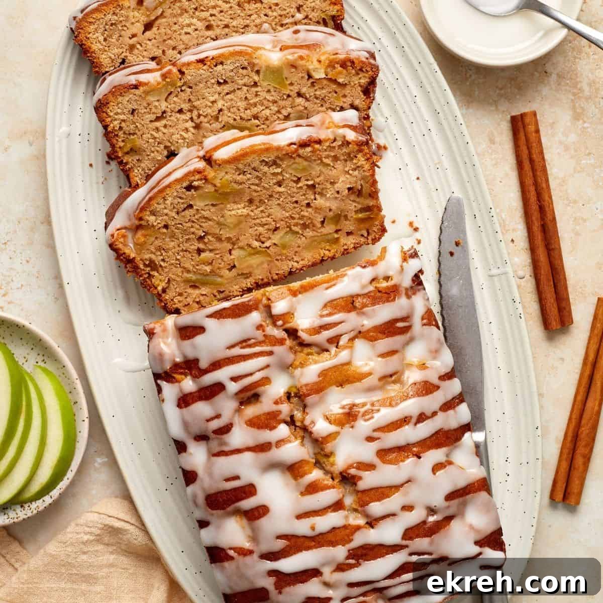 Apple Loaf Cake, with three slices cut, sitting on a white oval platter, with a knife on the side.