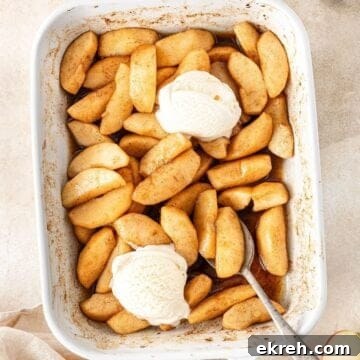 Rectangular white baking dish with the cooked Baked Apples, two scoops of ice cream and a spoon resting in the dish.