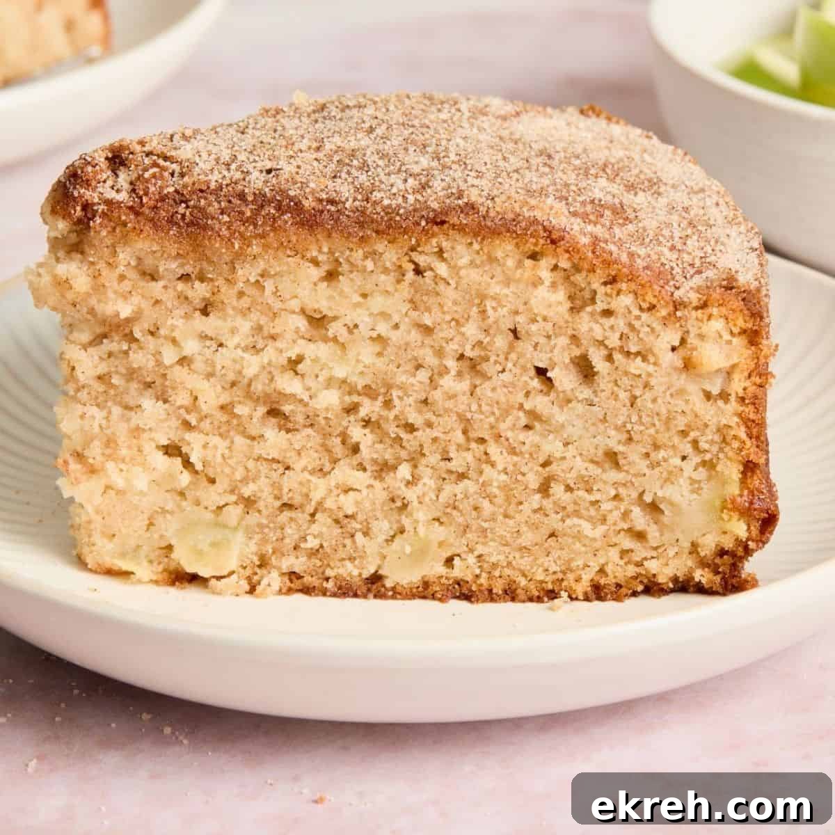 Slice of Apple Tea Cake, sitting on a small round white plate, with some other slices of cake in the background.