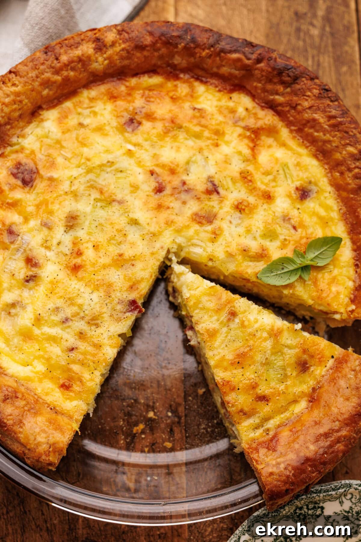 Quiche lorraine freshly baked with a slice cut out of it in a glass pie dish on a wood background.