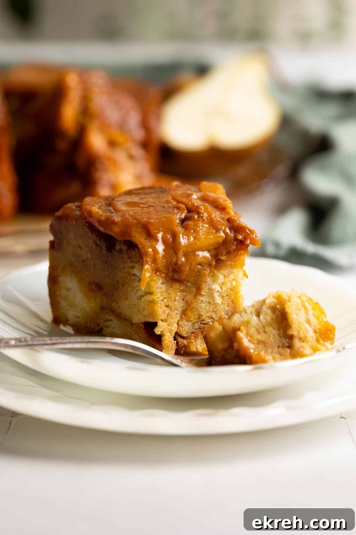 A slice of pear caramel bread pudding on a white plate with a bite on a fork.