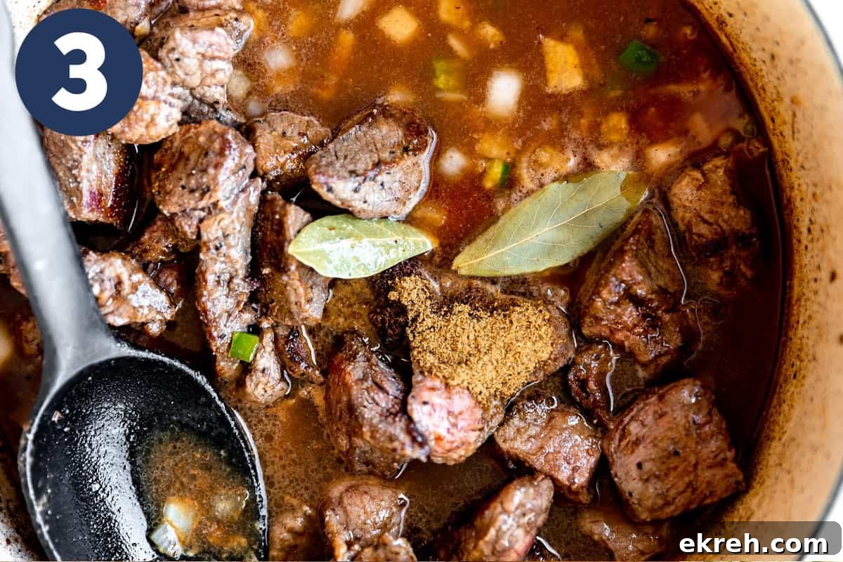 Dutch oven with stew meat in broth with bay leaves ready to simmer.