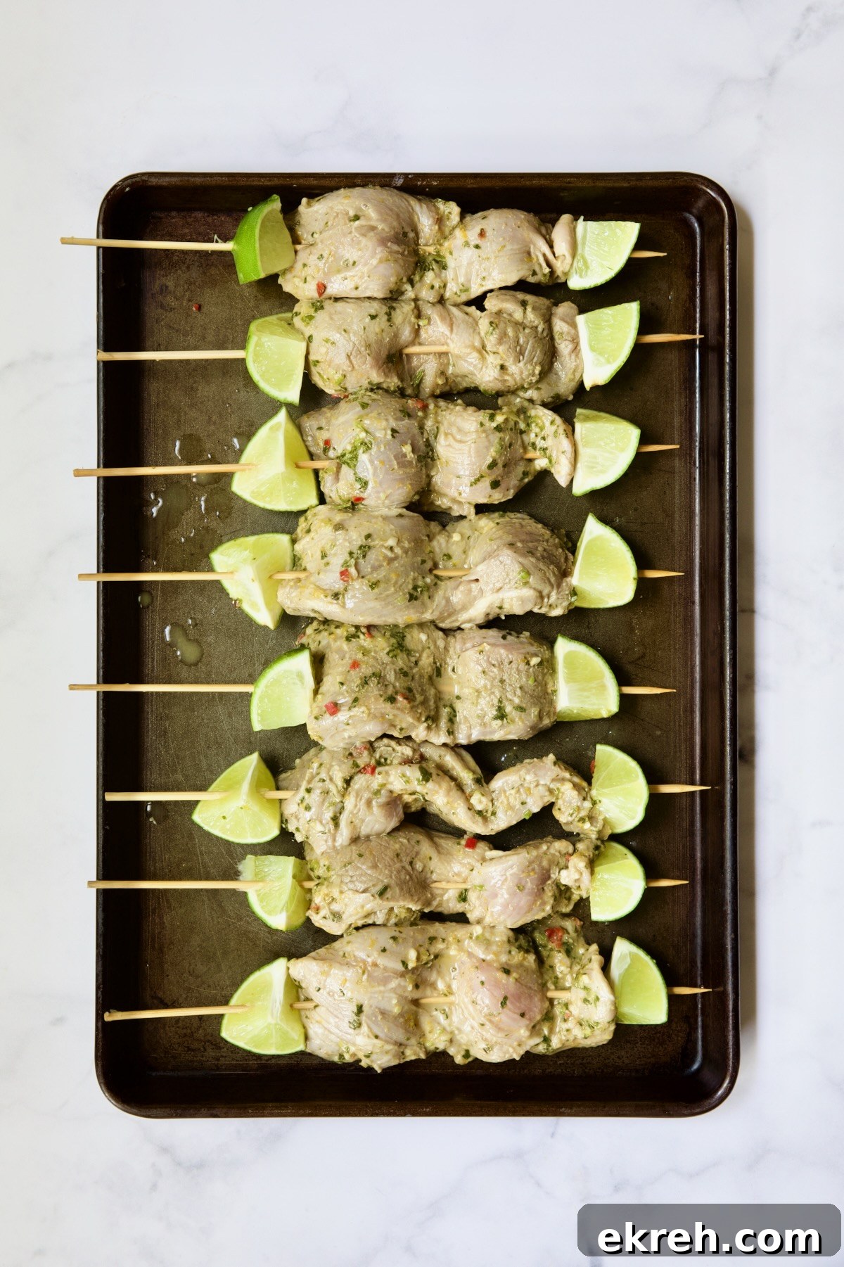 Grilled Citrus Mojo Pork Tenderloin Skewers 11 Uncooked pork tenderloin skewers on rimmed baking sheet.