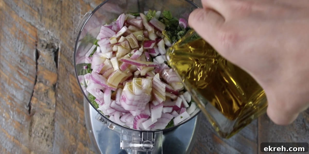 pouring olive oil into the food processor after adding the rest of the chimichurri ingredients