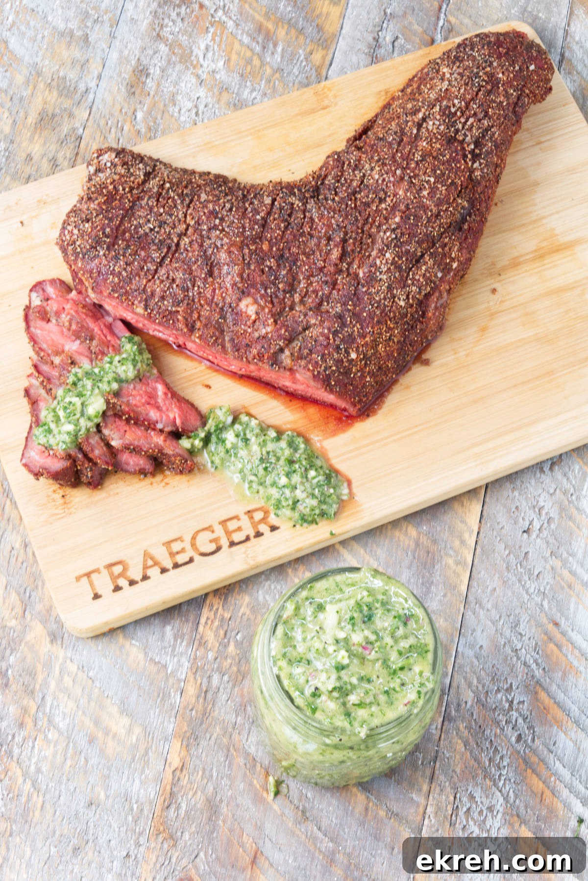 smoked tri-tip sliced on cutting board with cilantro chimichurri drizzled on top and chimichurri in mason jar