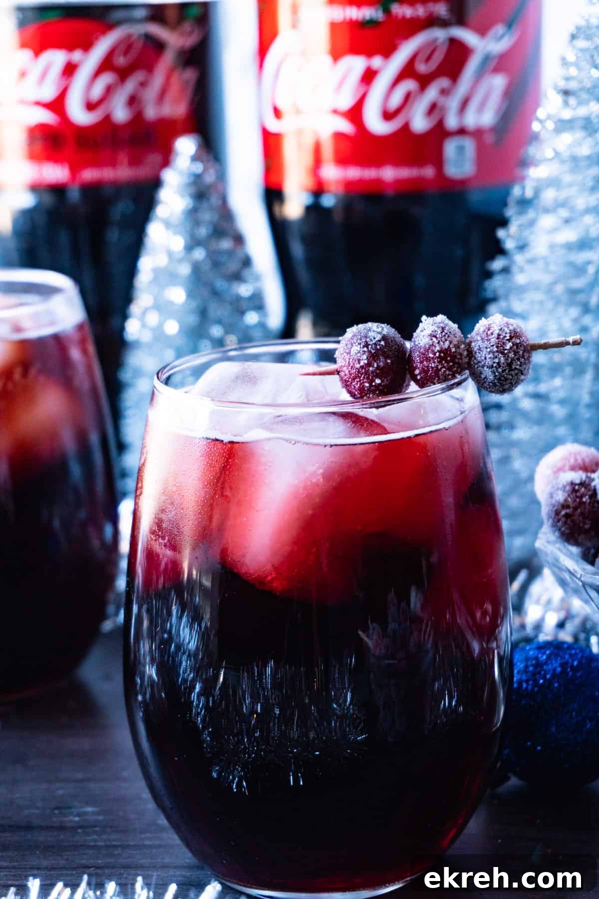 Quick Christmas Cocktail Recipe 2 Christmas drink in a clear glass with large ice cubes and a toothpick with sugared cranberries on it to garnish the drink.