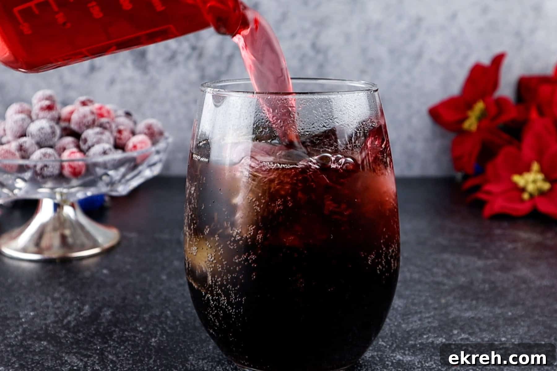 Quick Christmas Cocktail Recipe 7 Adding cranberry juice to a glass with festive decorations in the background.