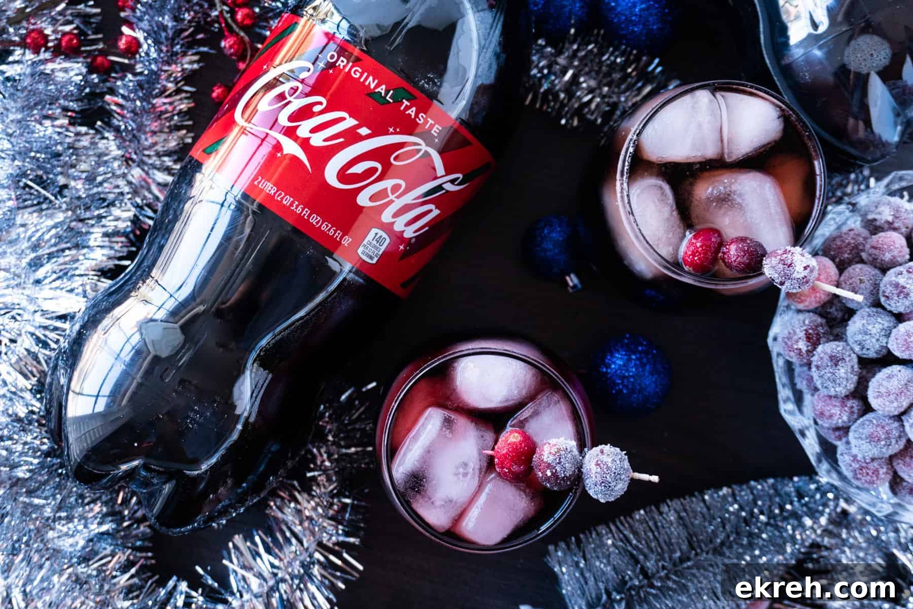 Quick Christmas Cocktail Recipe 9 Two glasses of Christmas Drink with sugared cranberries as garnish, next to a 2L bottle of Coca-Cola. Festive holiday decorations are all around the glasses and the soda bottle.