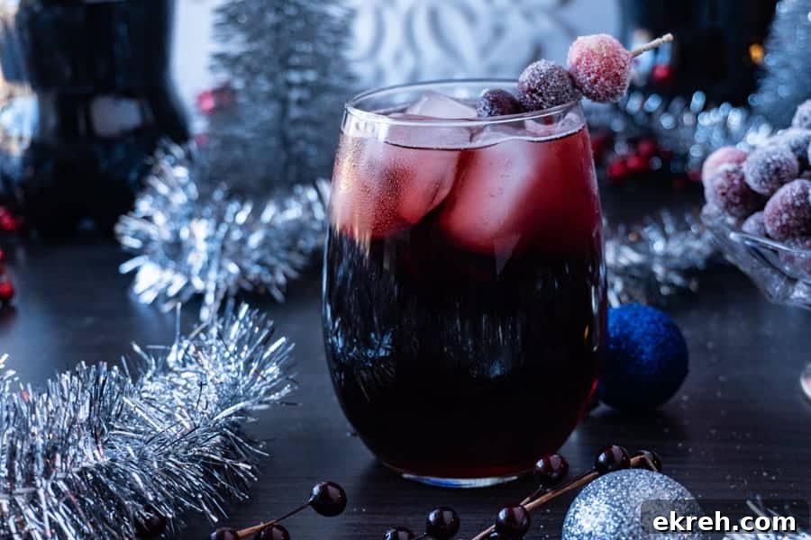 Quick Christmas Cocktail Recipe 10 Easy Holiday Drink in a clear glass surrounded by blue and silver holiday decorations.